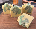 Four bars of soap with green swirls on a wooden cutting board in a kitchen setting.