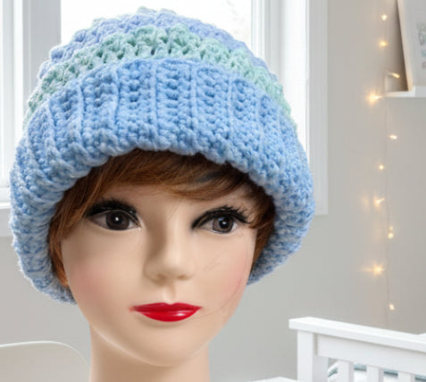 Mannequin head wearing a blue and green crocheted hat with a blurred background
