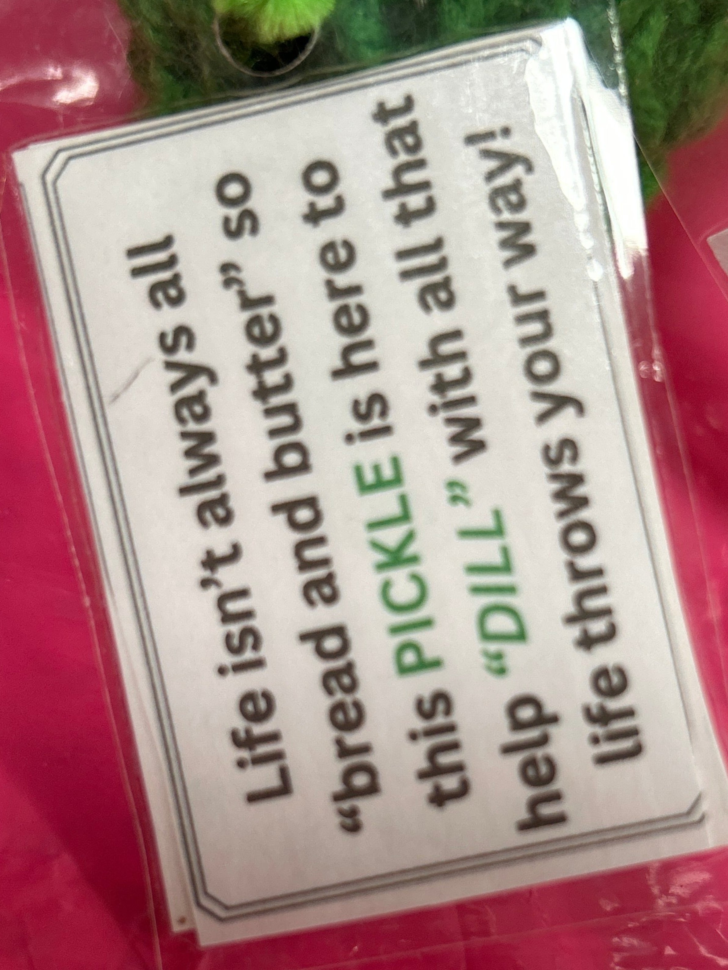 Green pickle toy with humorous text tag on pink background