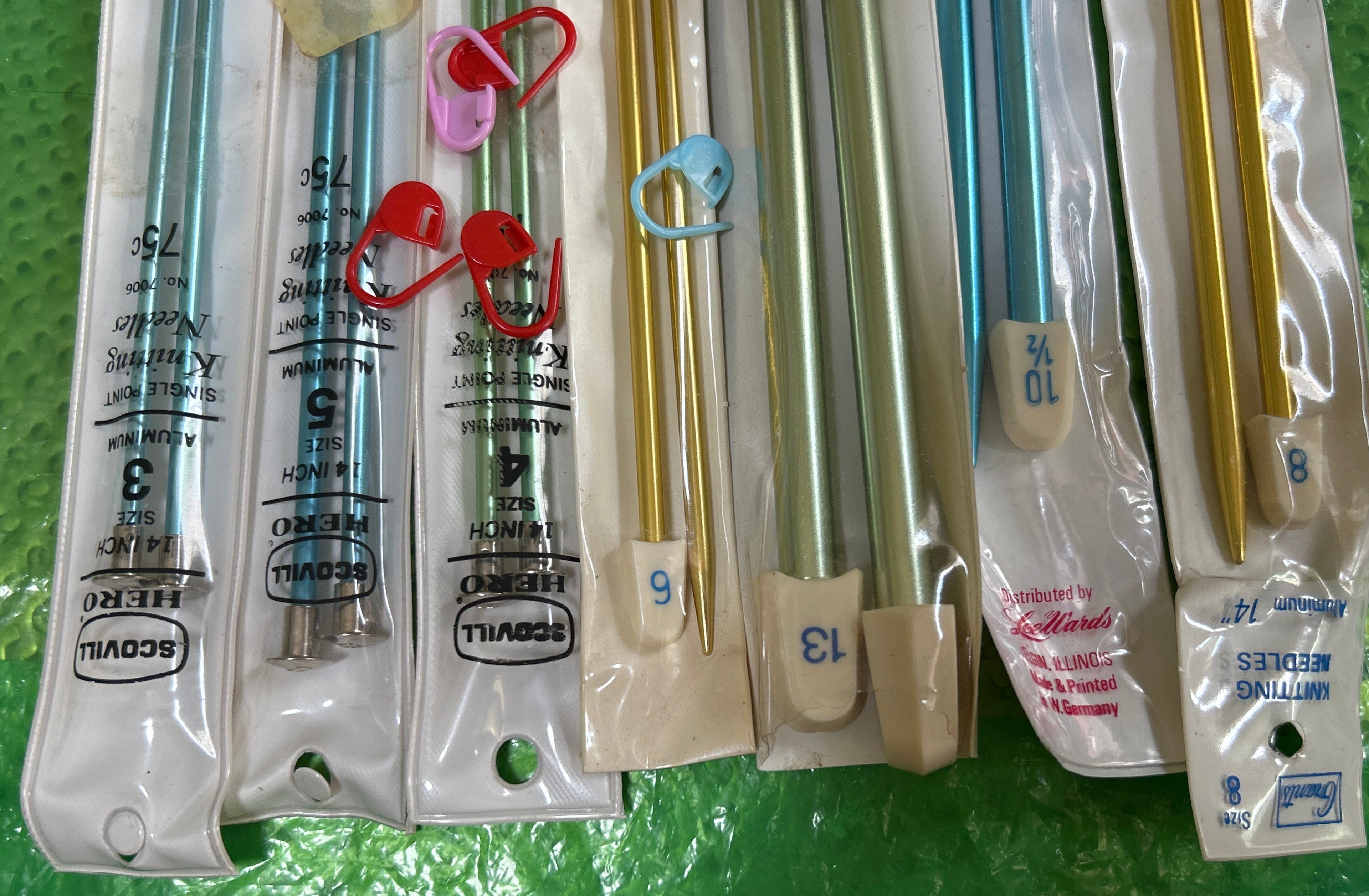 Set of metal knitting needles in packaging on a green surface