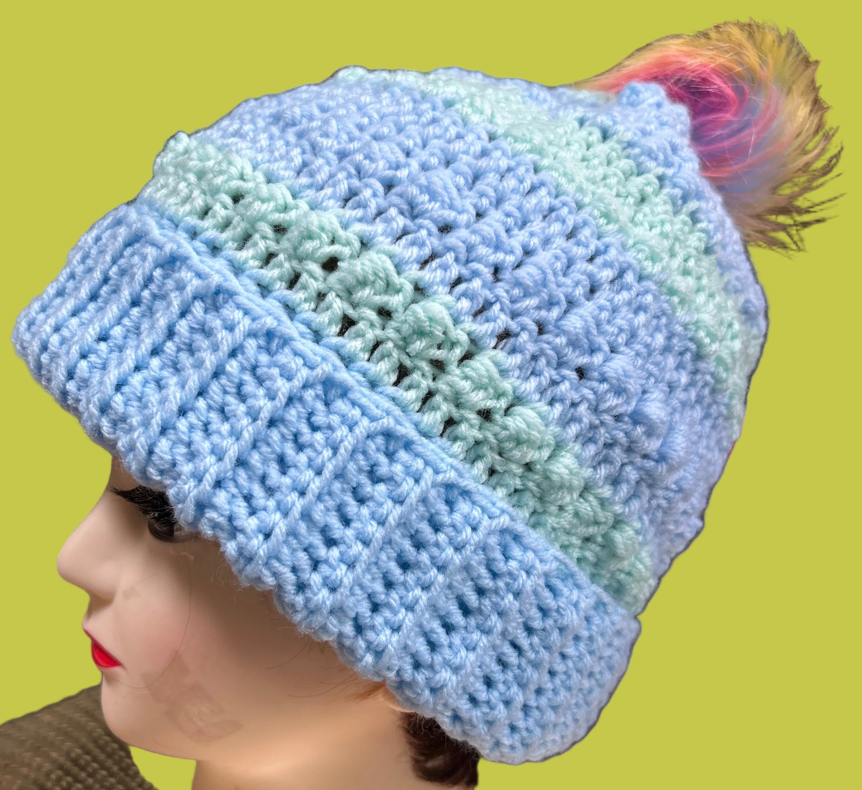 Blue and green knitted beanie on a mannequin head with a blurred background