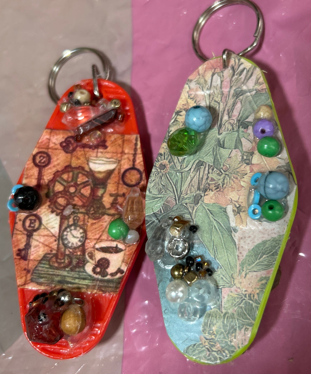 Two decorative keychains on a reflective surface with a pink and gray background