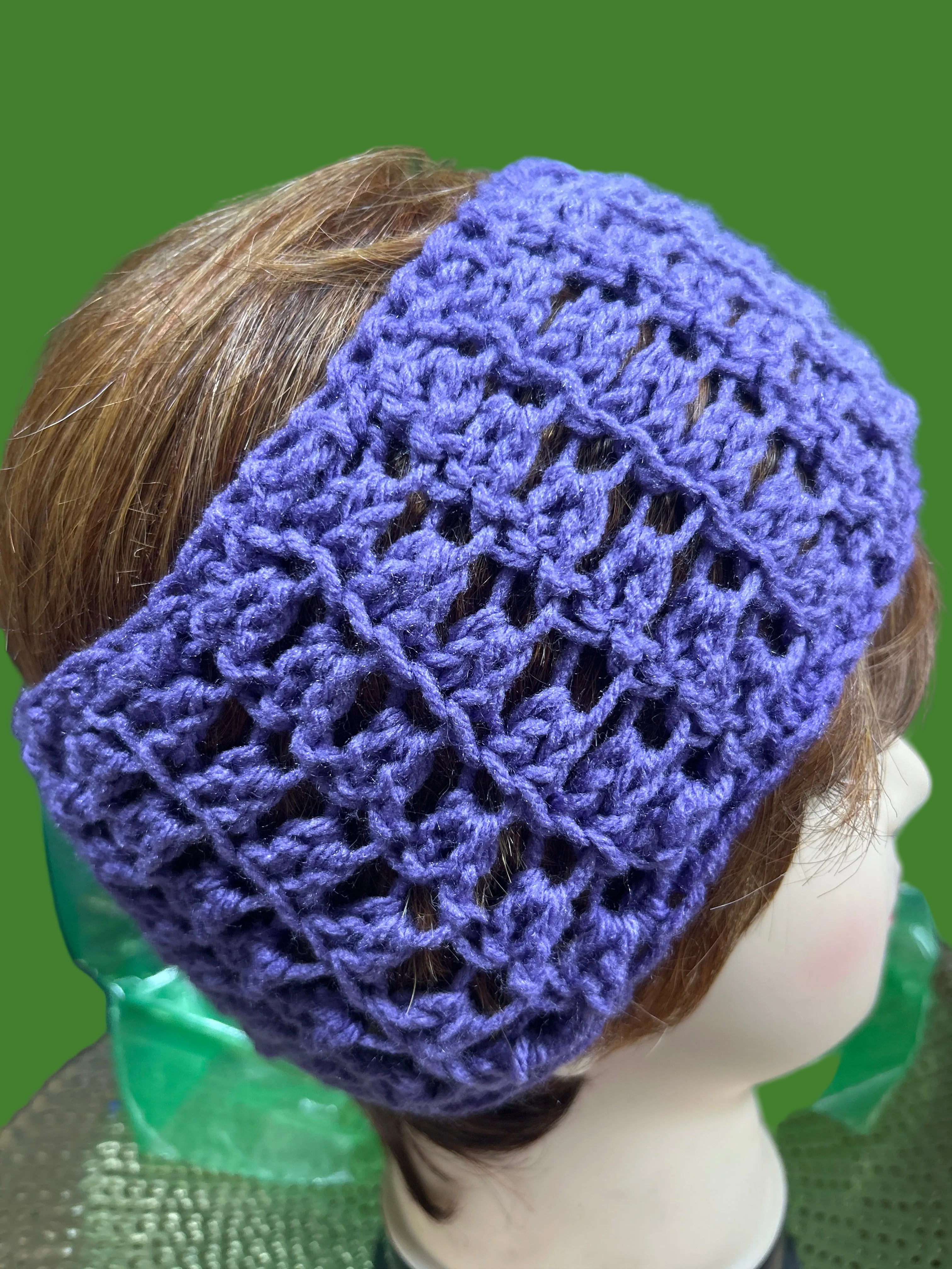 Purple crocheted headband on a mannequin head with a green background