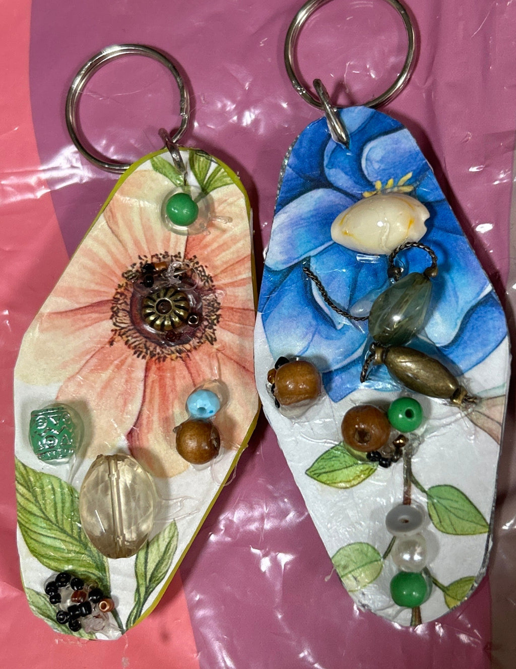 Two decorative keychains with floral designs on a pink surface.