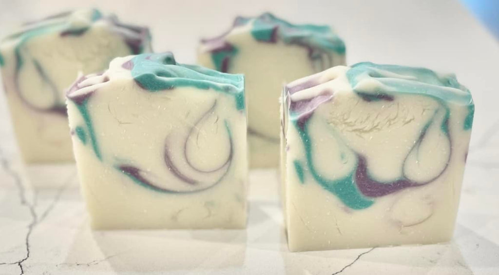 Five small soap bars with a marbled design on a marble surface.