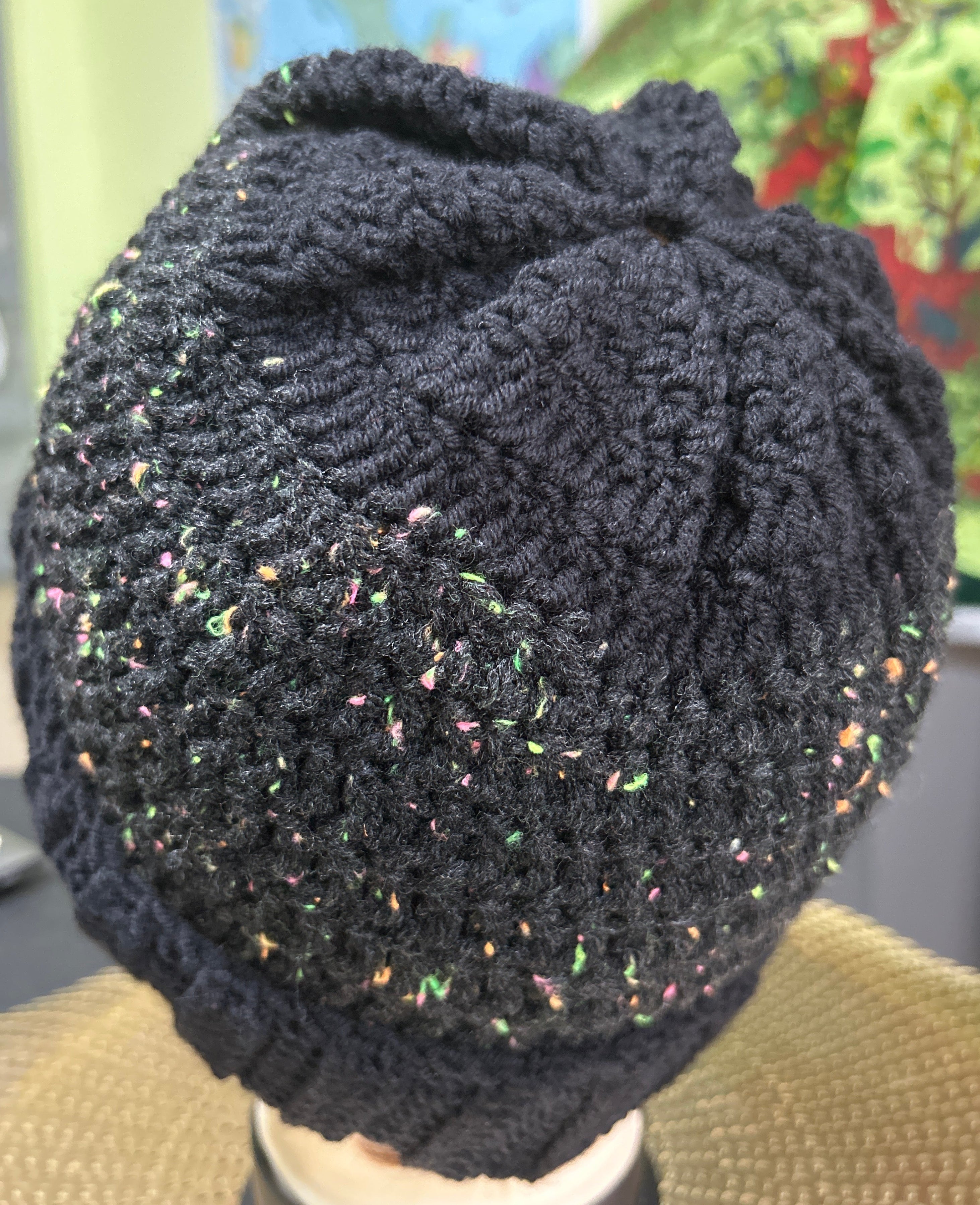 Black textured knitted hat held by a hand with a blurred background