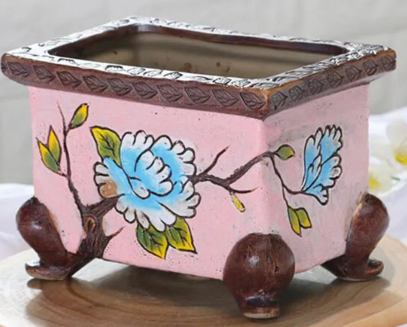 Decorative pink ceramic planter with floral design on a white background