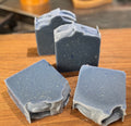 Four blue soap bars on a wooden cutting board in a kitchen setting.