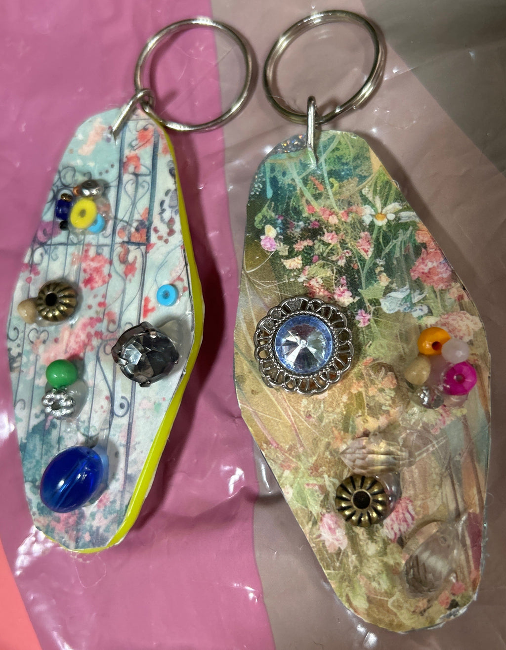 Two decorative keychains with floral patterns and colorful beads on a pink surface.