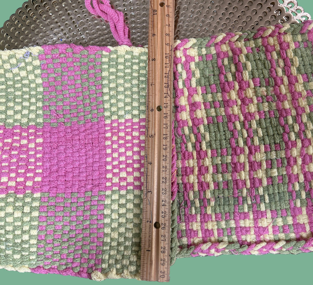 Woven fabric with a checkered pattern in pink and green, measured against a circular metal object.