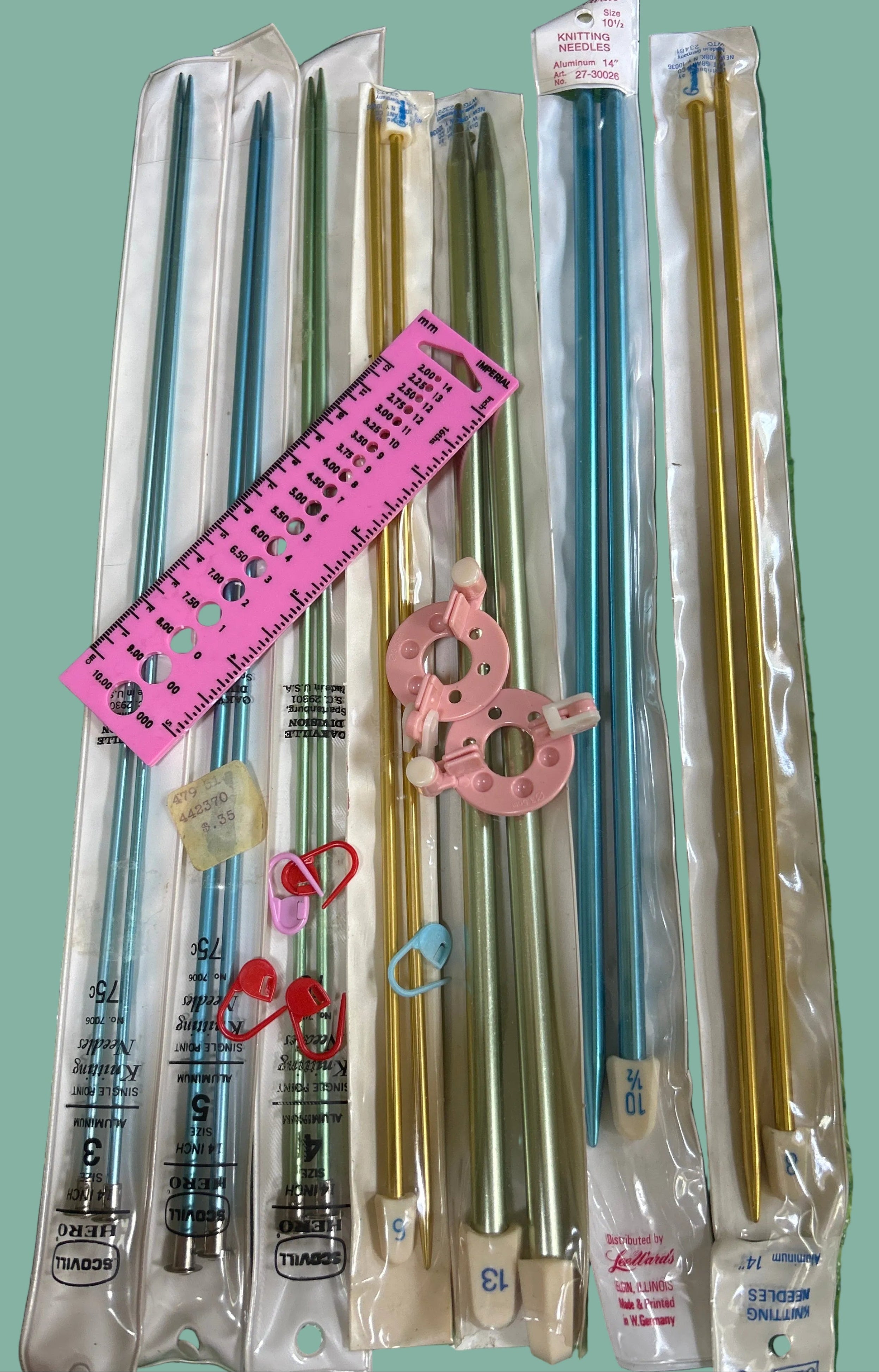 Set of metal knitting needles in packaging on a green surface