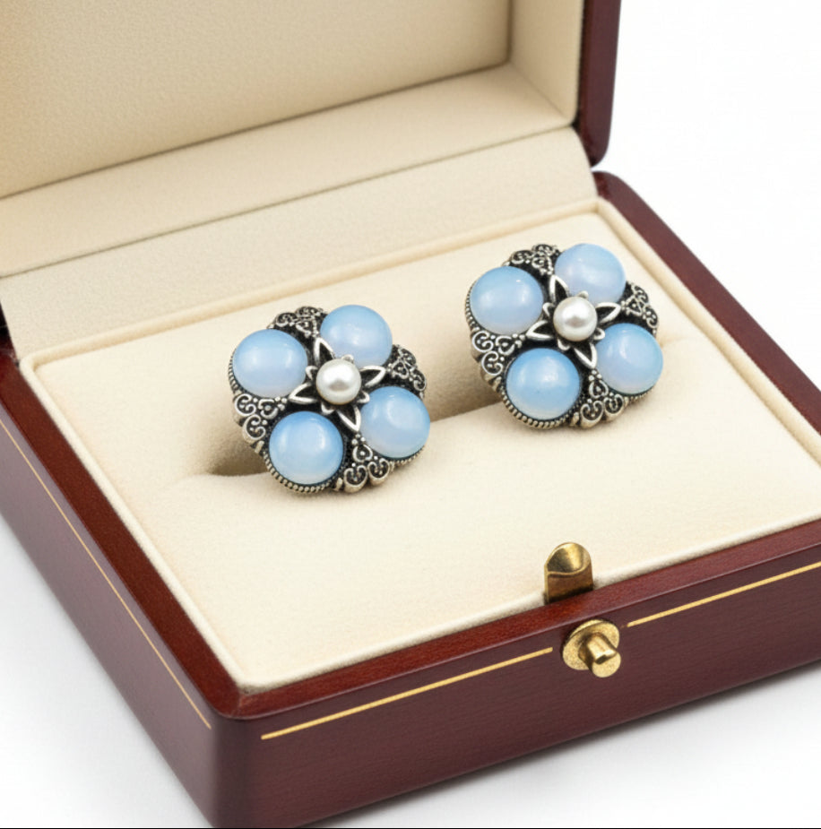 Pair of earrings with blue gemstones and pearl centers on a white background