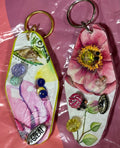 Two decorative keychains on a pink surface with a clear plastic overlay.