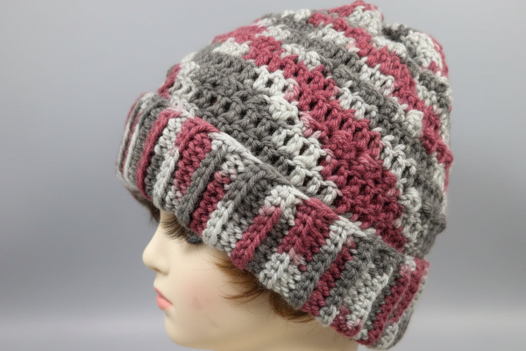 Gray and pink knitted glove held by a hand against a pink background