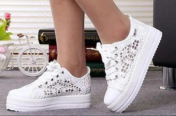 White lace-up sneakers worn by a person with a blurred indoor background