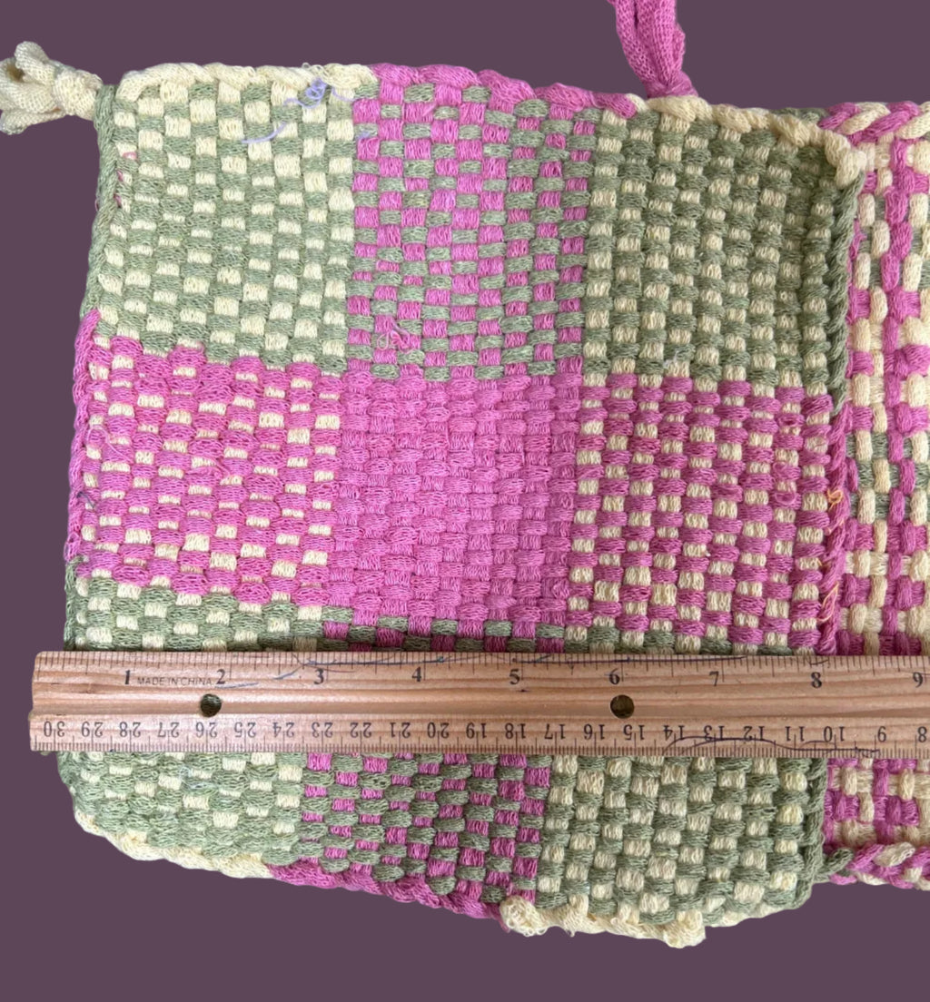 Handwoven pouch with pink and green pattern on a textured surface, with a ruler for scale.