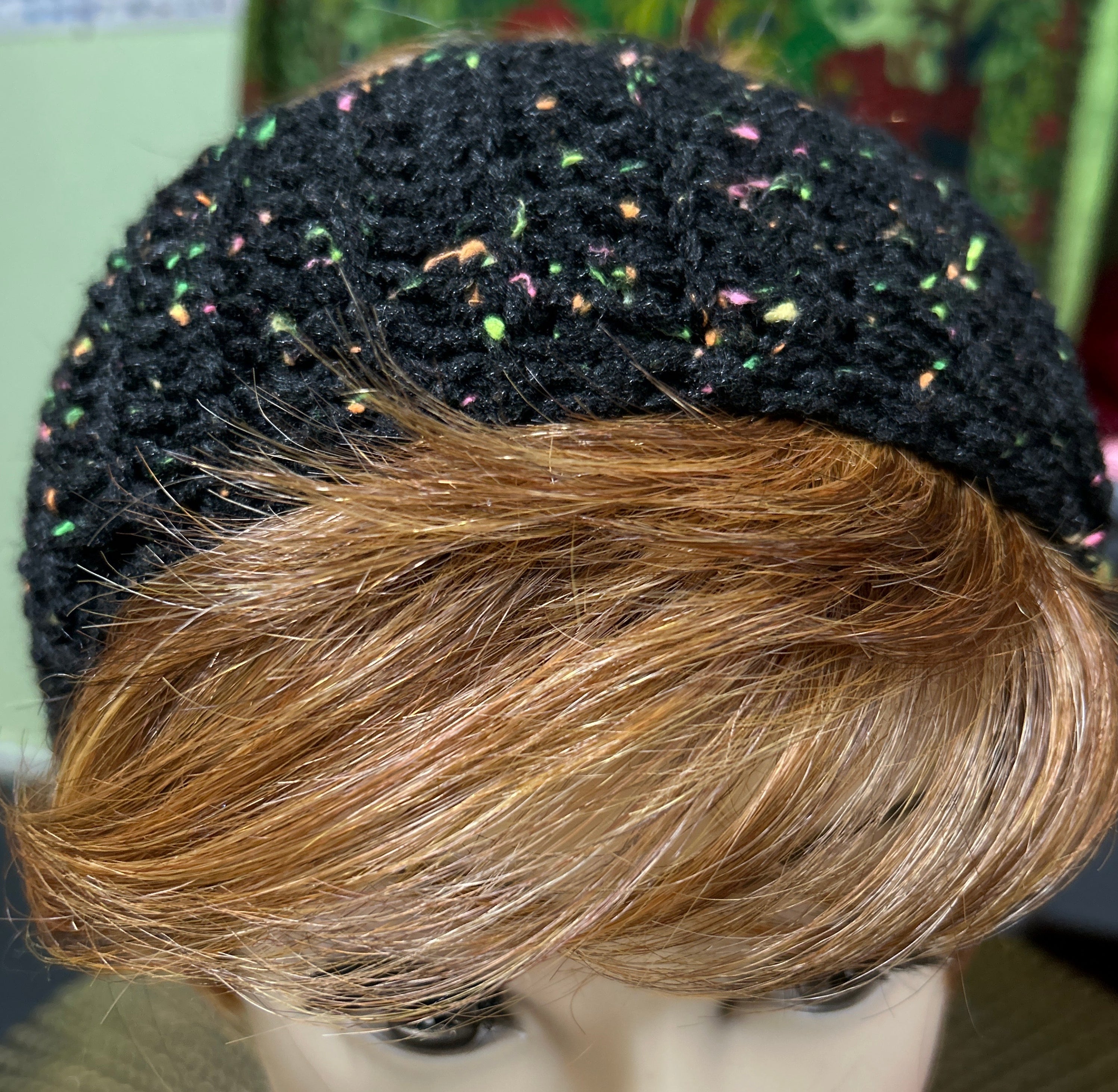 Mannequin head with black textured headband and blonde hair against a colorful background