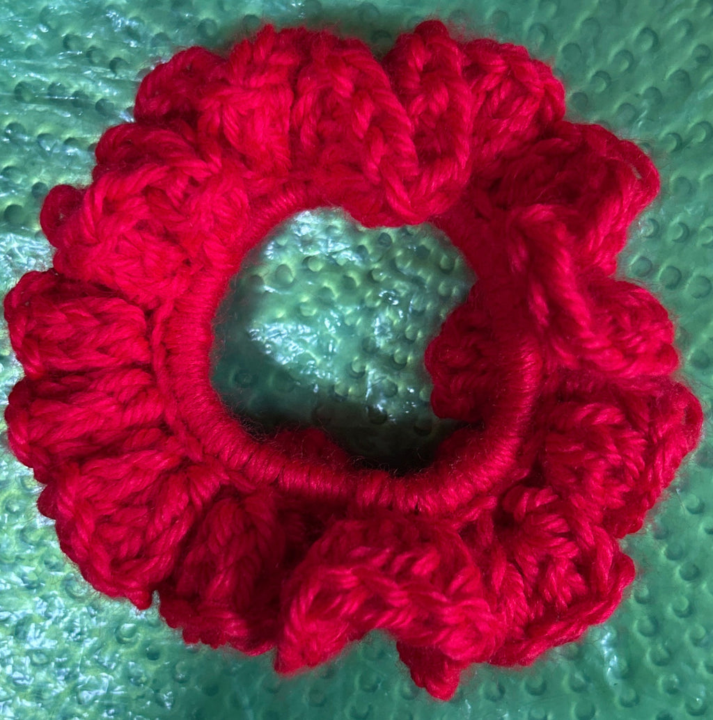 Red knitted scrunchie on a textured green surface