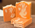 Three orange and white soap bars on a wooden surface with a blurred background