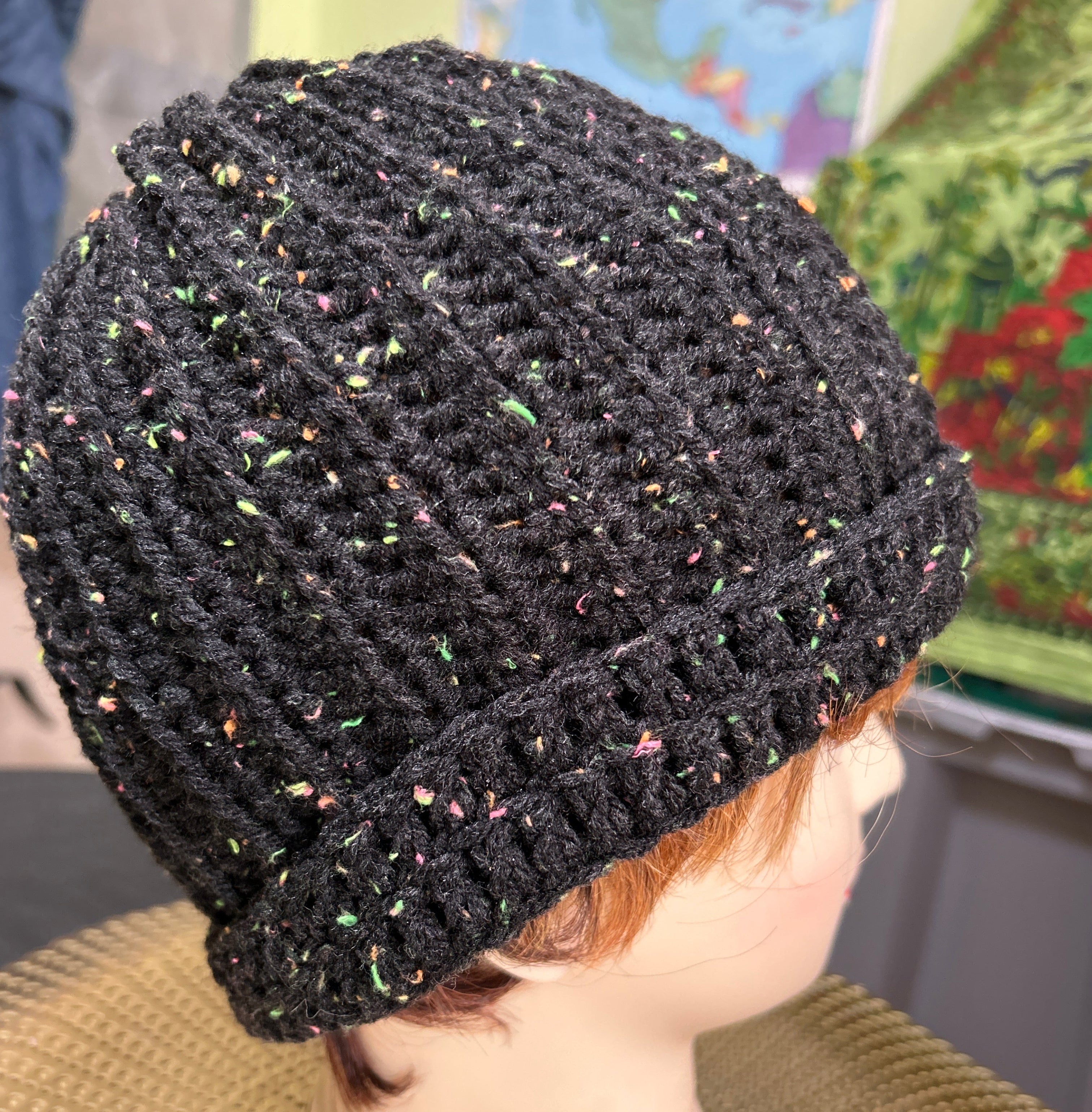 Black textured beanie held by a hand with a blurred background