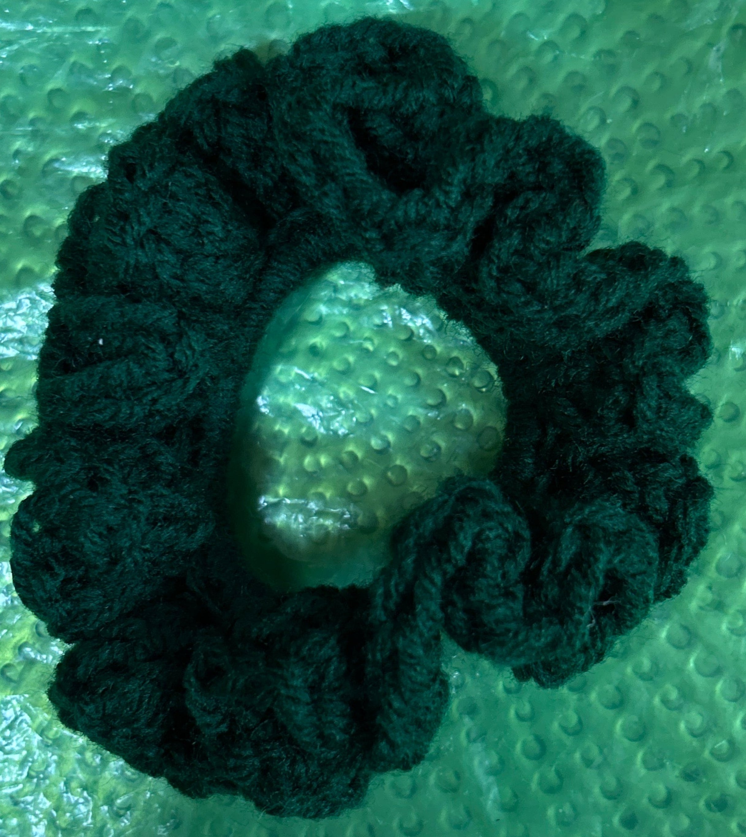 Dark green scrunchie on a textured green surface
