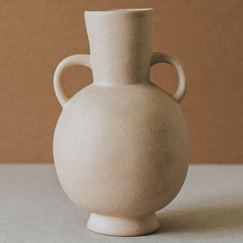 Beige ceramic vase with two handles on a neutral background