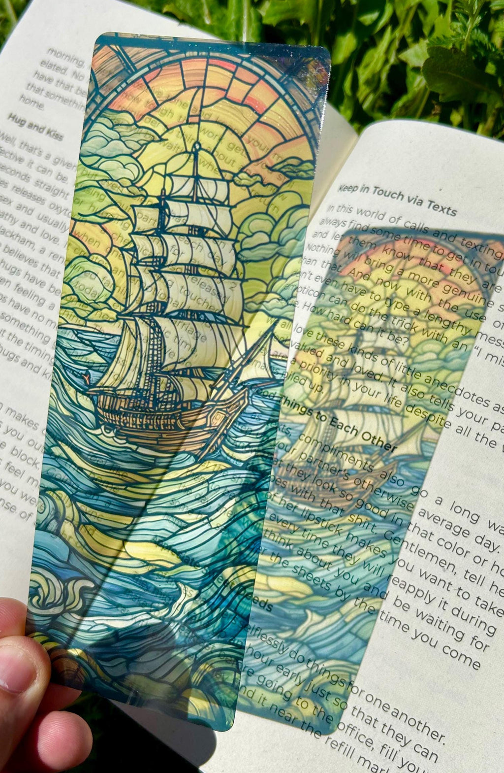 Colorful ship-themed bookmark on an open book with greenery in the background