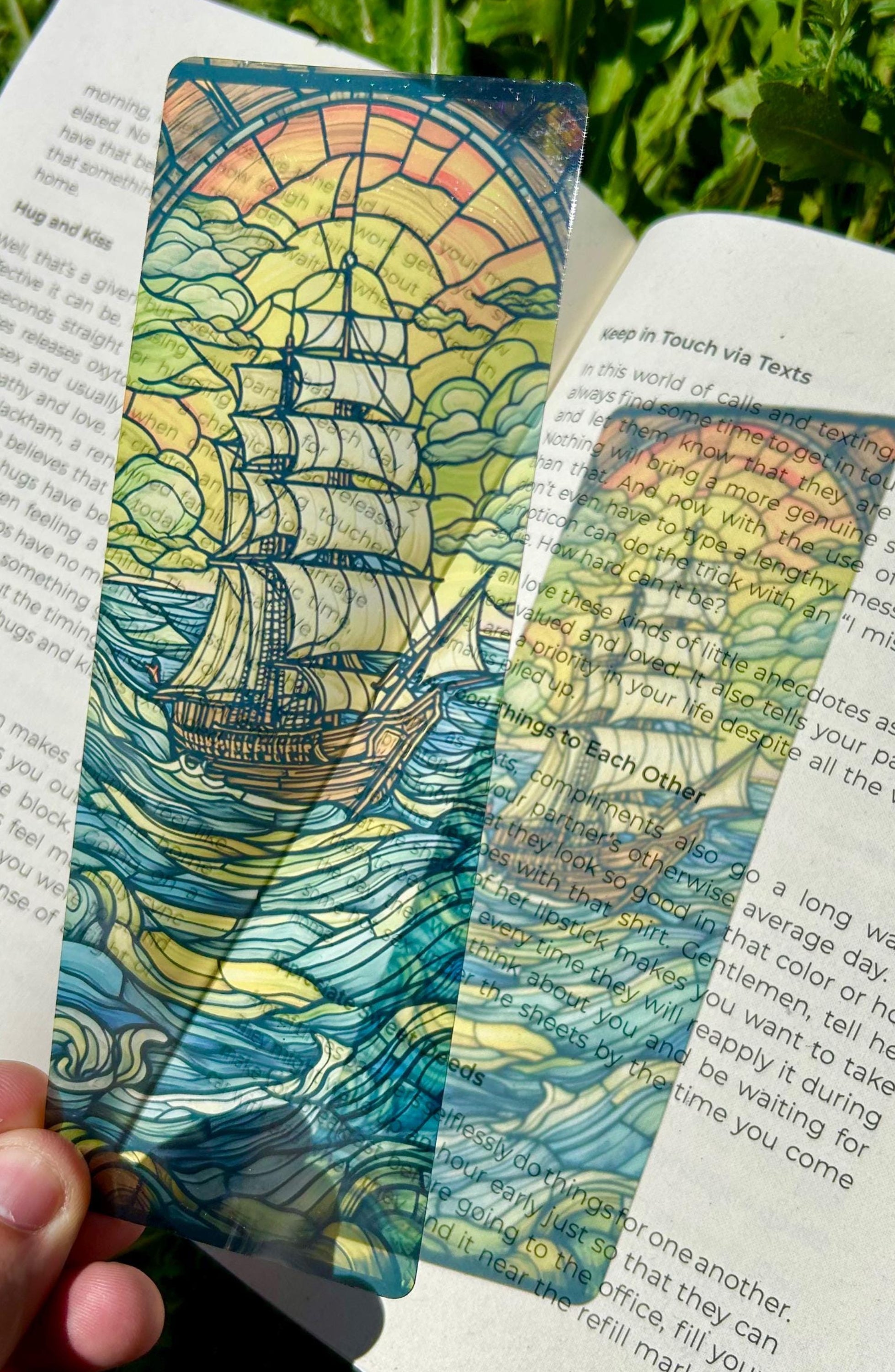 Colorful ship-themed bookmark on an open book with greenery in the background