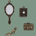 Set of four vintage-style bronze charms including a mirror, book, high heel shoe, and suitcase on a white background.
