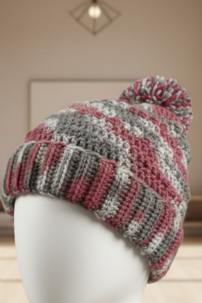 Close-up of a textured knitted item with a pink and gray pattern on a blurred background.