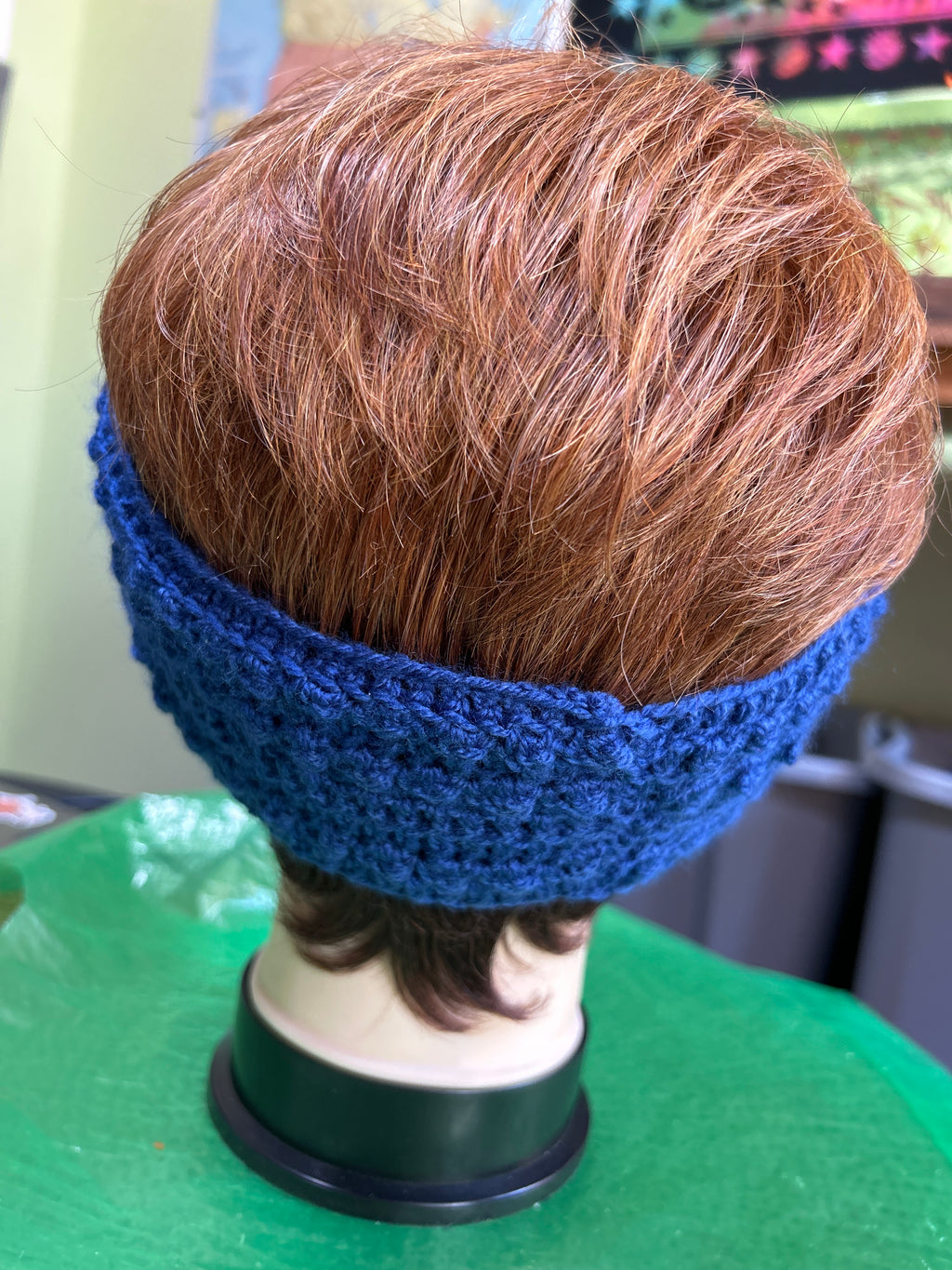 Mannequin head with brown hair and a blue headband on a green surface.