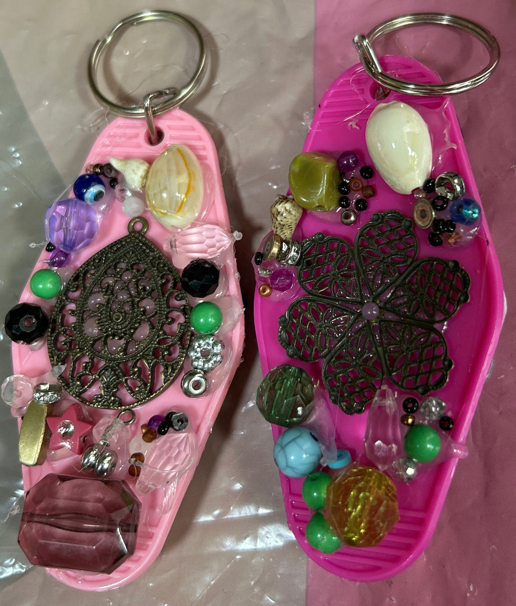 Two pink keychains with decorative elements on a reflective surface
