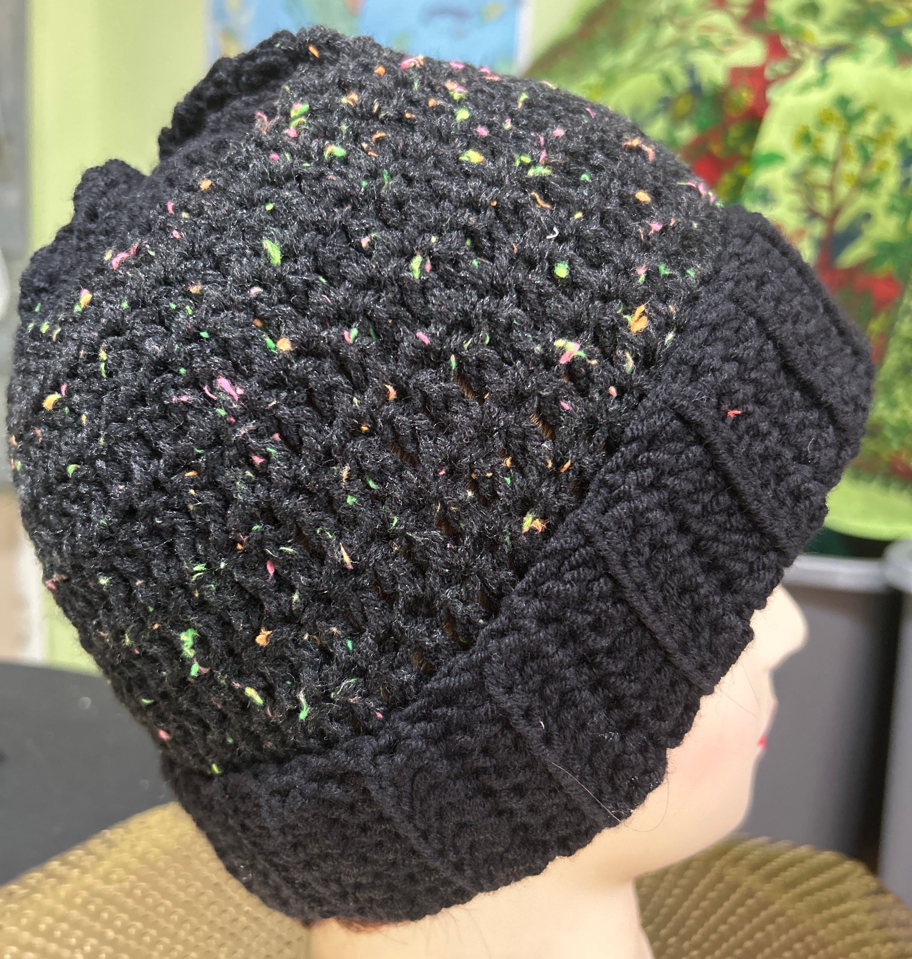 Black textured knitted hat held by a person with a colorful background