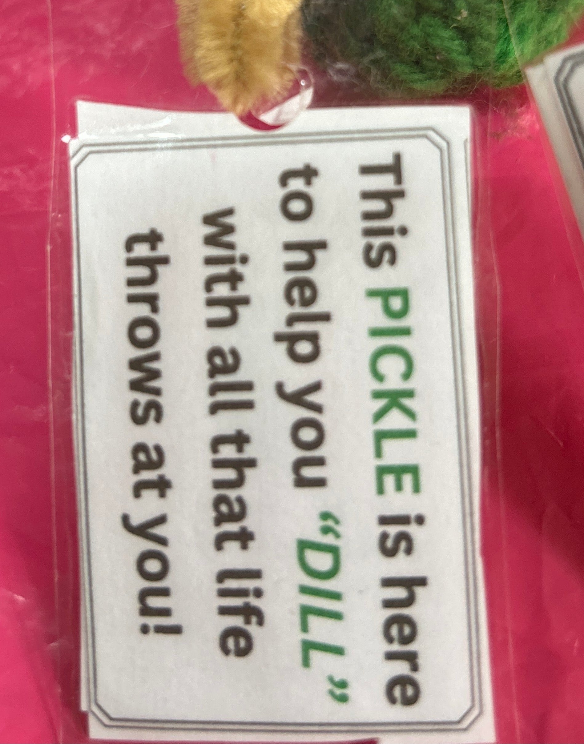 Green pickle-shaped toy with a red button on a pink background