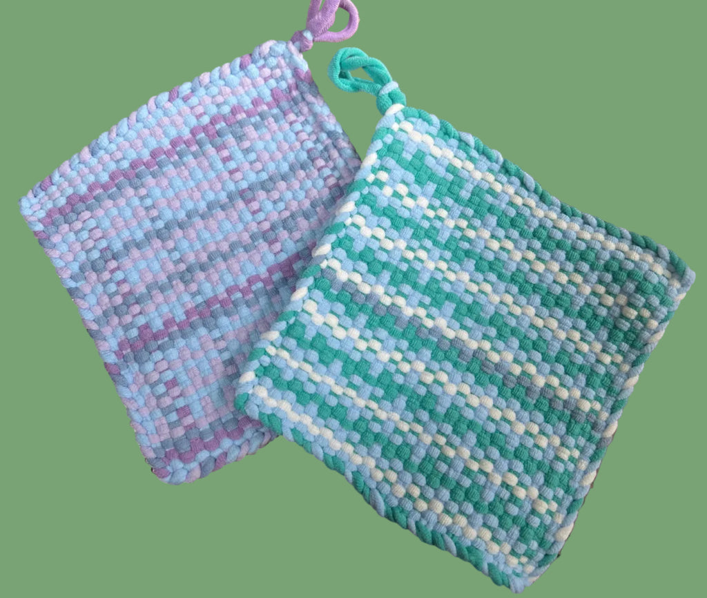 Two woven potholders, one purple and one green with white, on a green background.