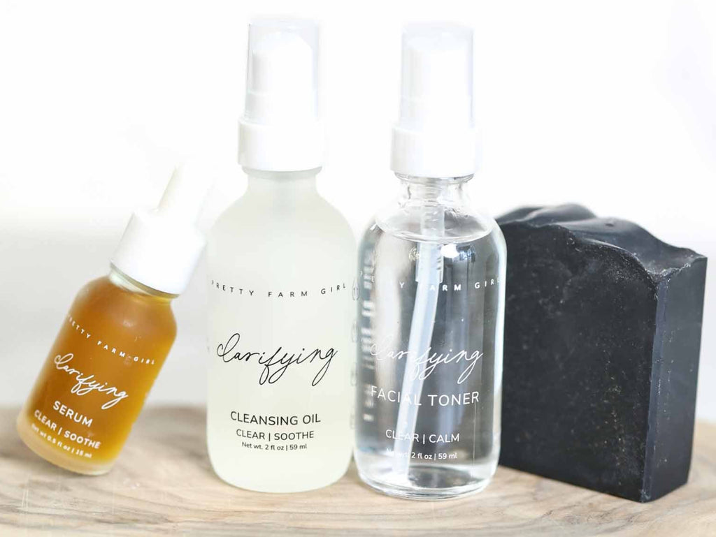 Set of skincare products including serum, cleansing oil, toner, and soap on a wooden board.