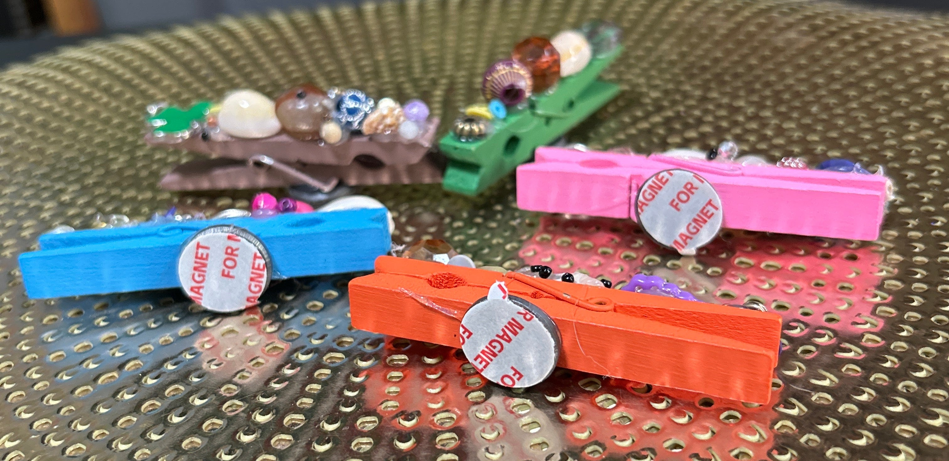 Colorful clothespins with decorative elements attached to a textured surface.