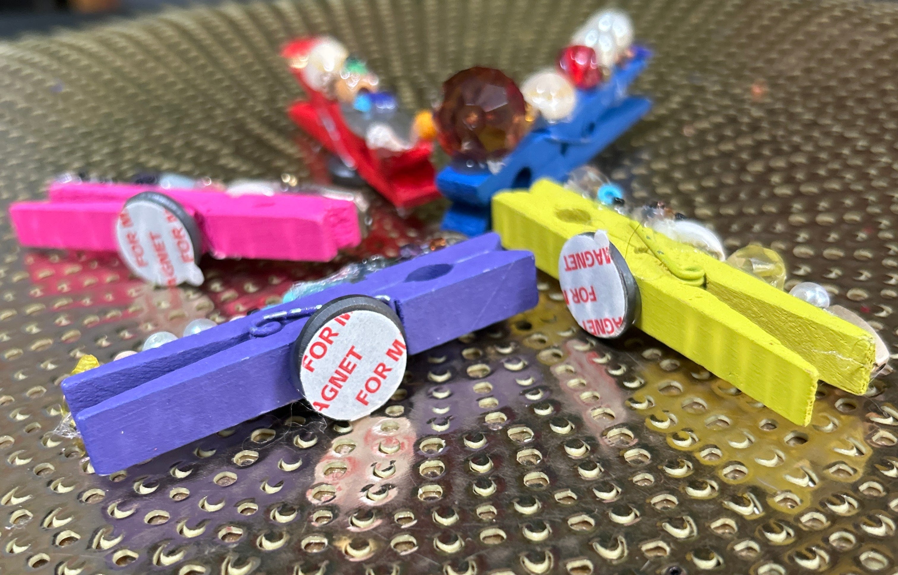 Colorful clothespins with decorative elements attached to a textured surface