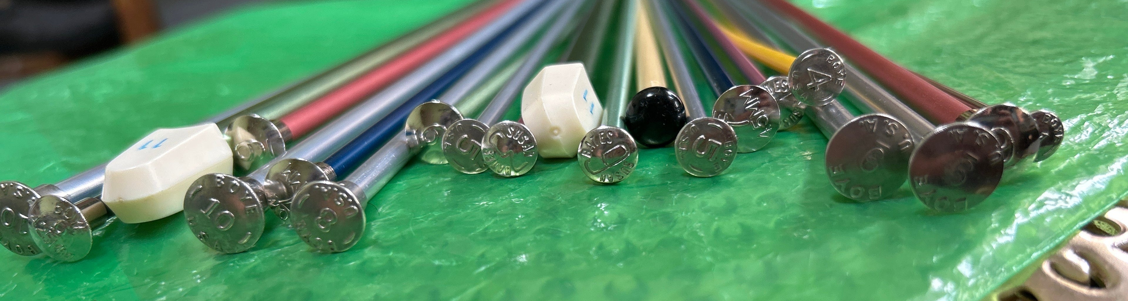 Set of metal knitting needles on a green mat with blurred background