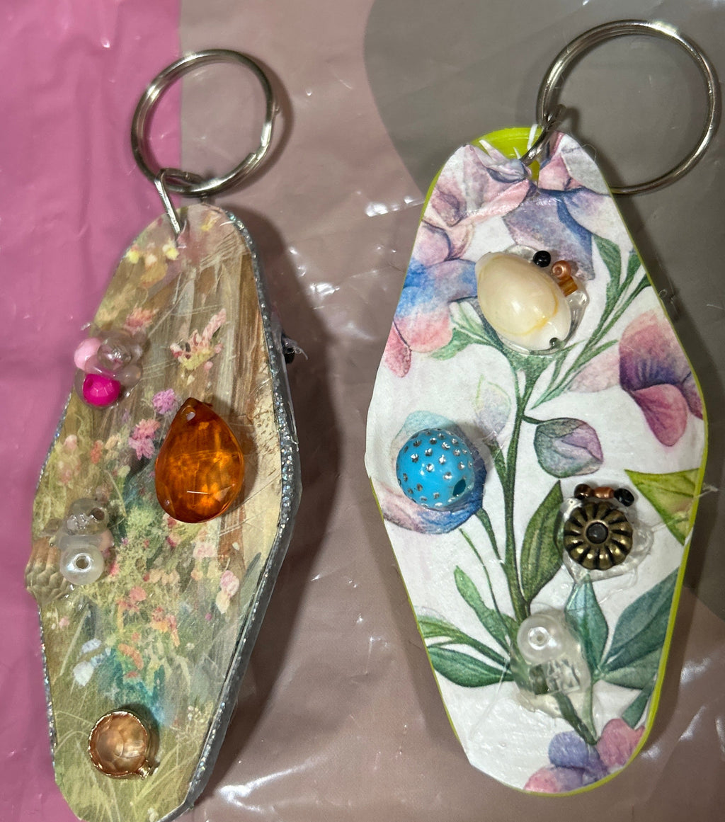 Decorative keychains with floral designs and beads on a reflective surface.