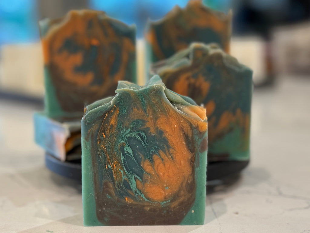 Three green and orange marbled soap bars on a light surface with a blurred background