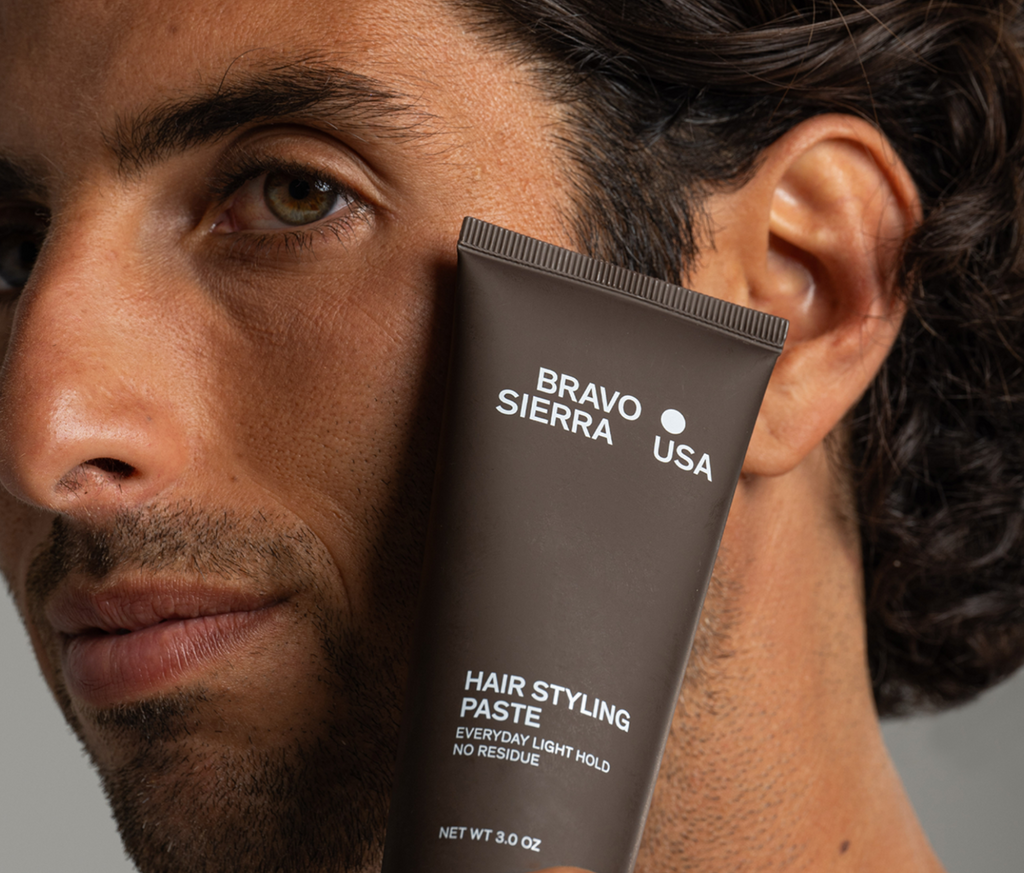 Man holding a bottle of hair styling paste against a gray background