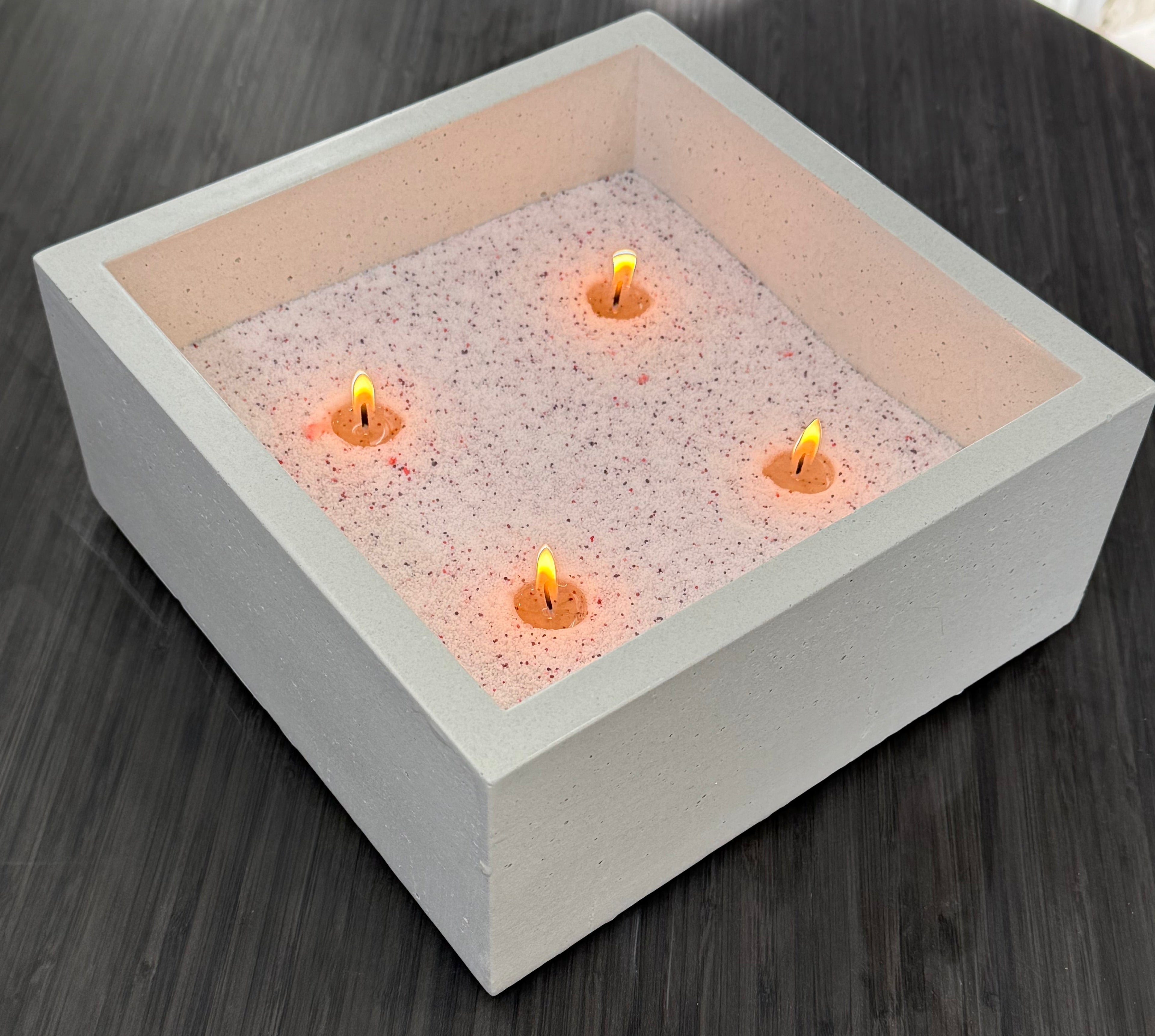 Square fire pit with glowing candles on a wooden surface