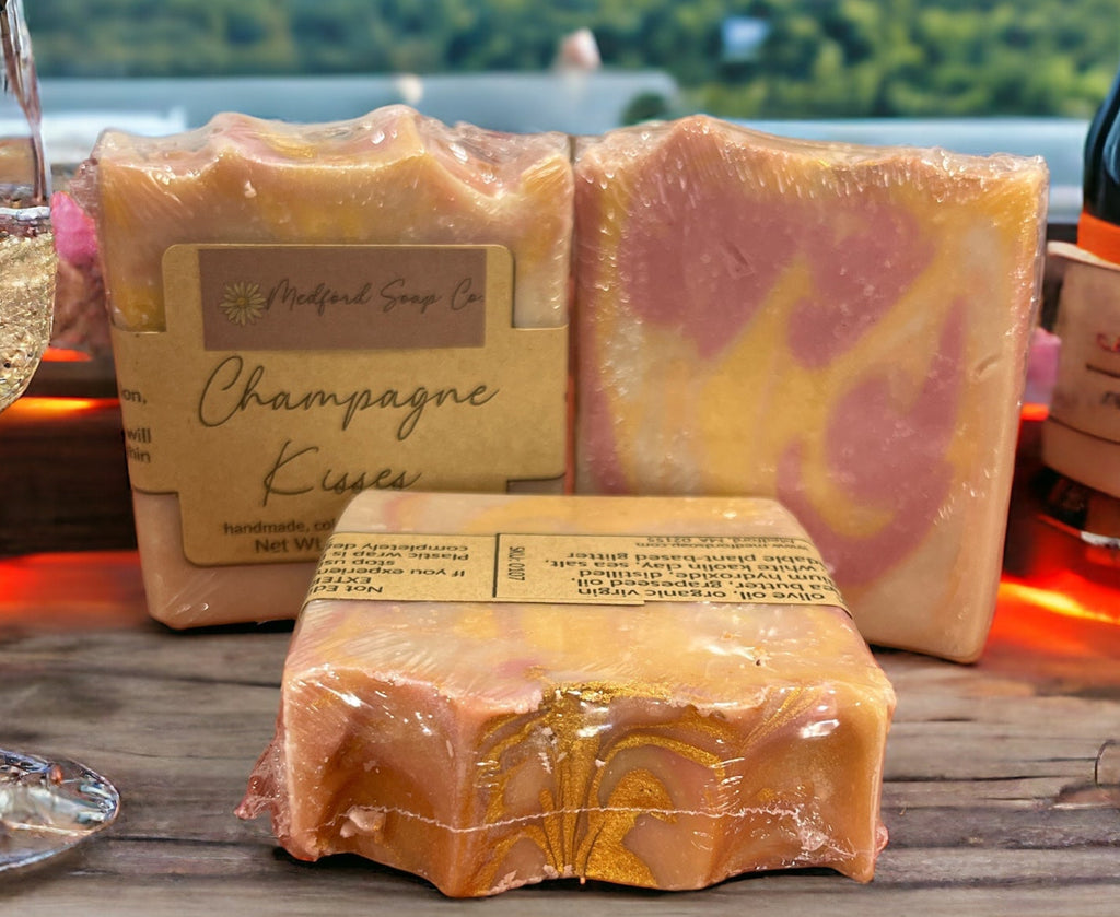 Three wrapped soaps with visible branding on a wooden surface, with a scenic background.
