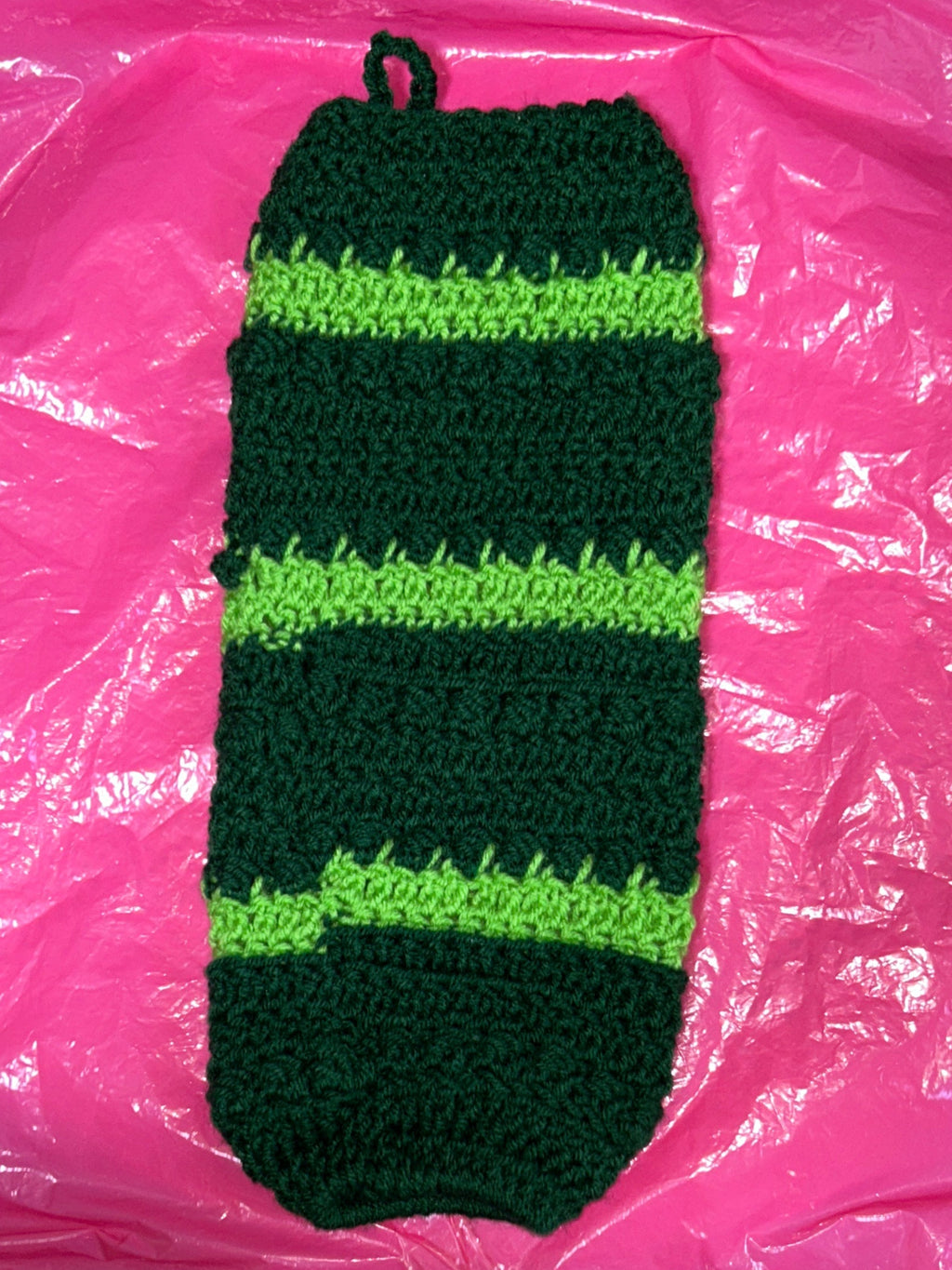 Green and black striped knitted item on a pink plastic bag with a patterned object in the background.