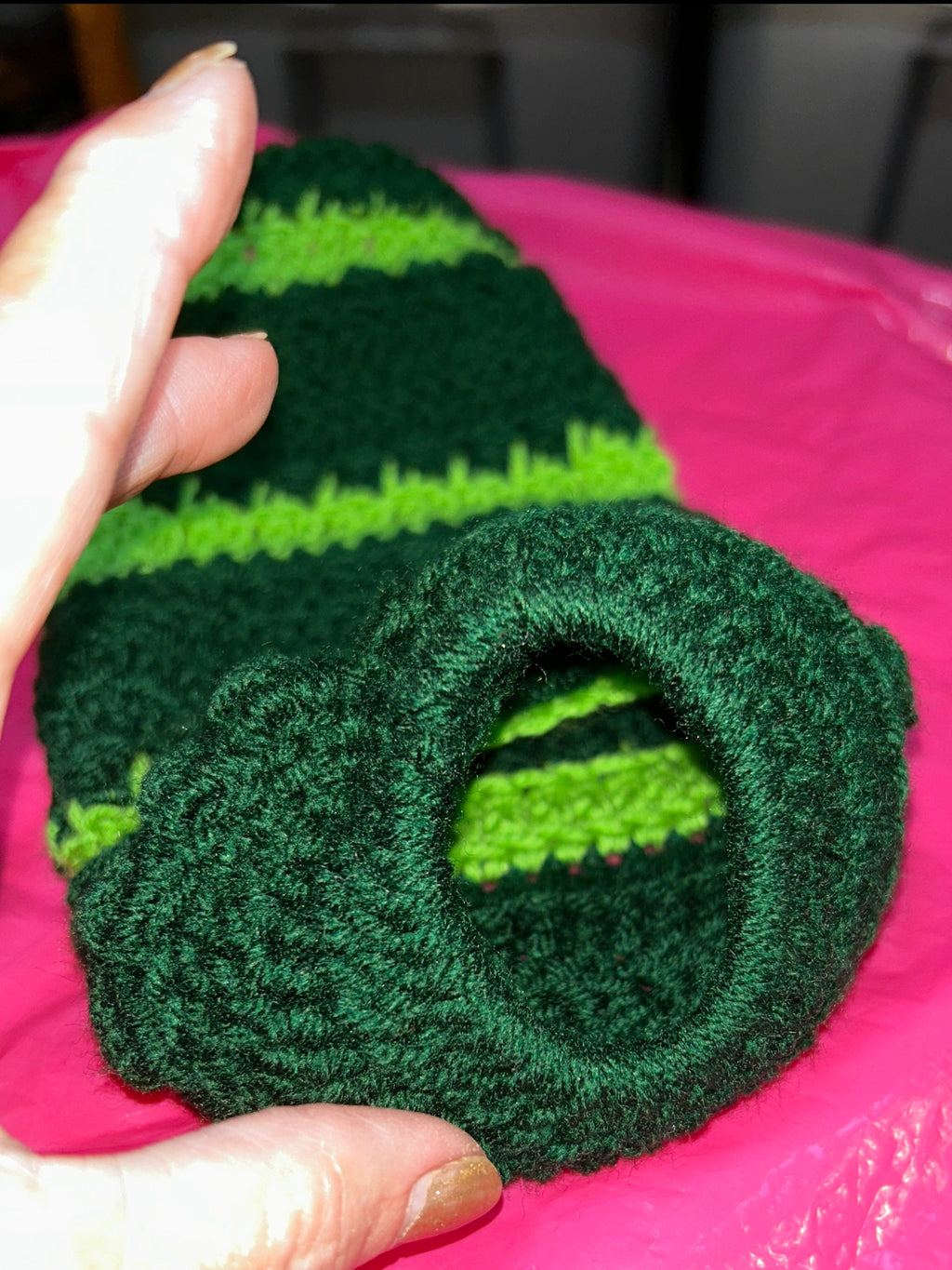 Green and black striped sock held in front of a pink plastic bag