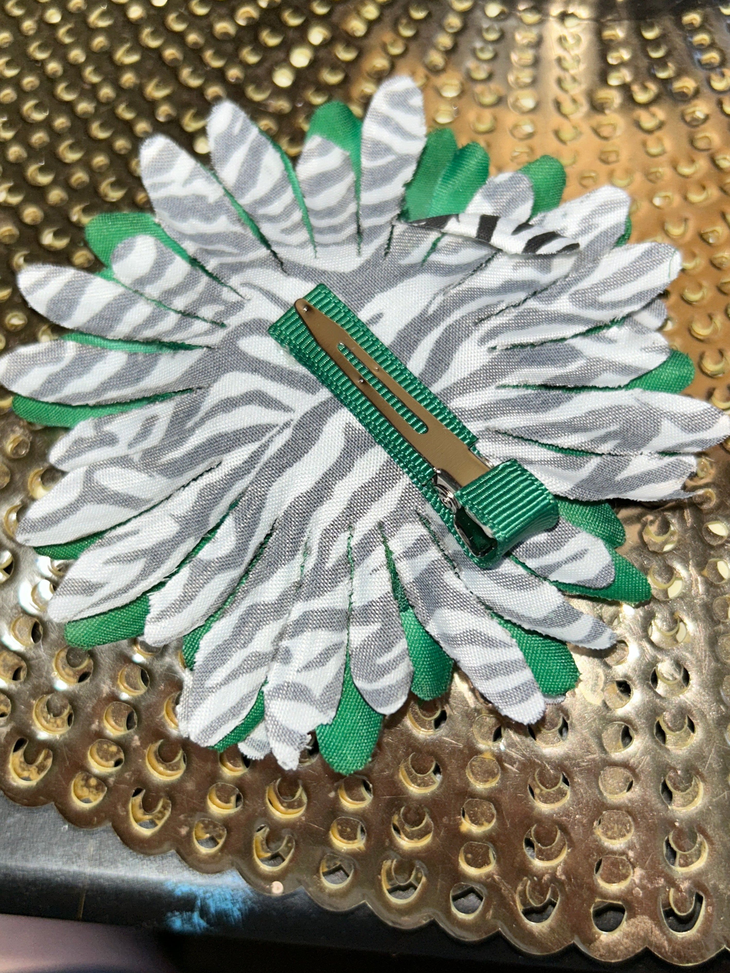 Decorative brooch with white and green floral design on a textured gold and black background