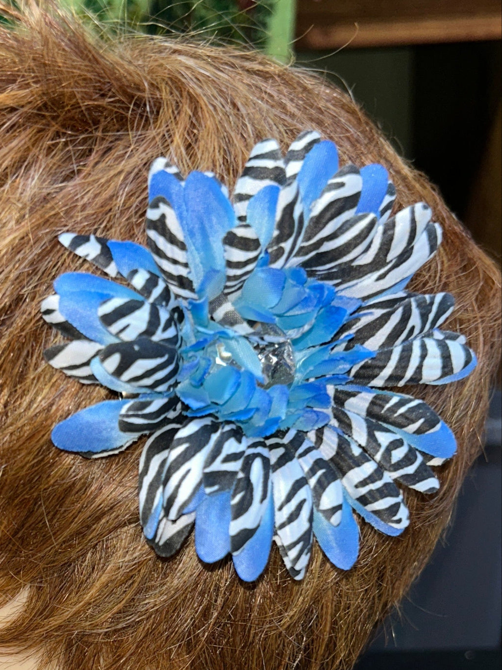 Mannequin head with a blue and black flower hair accessory on a textured surface.