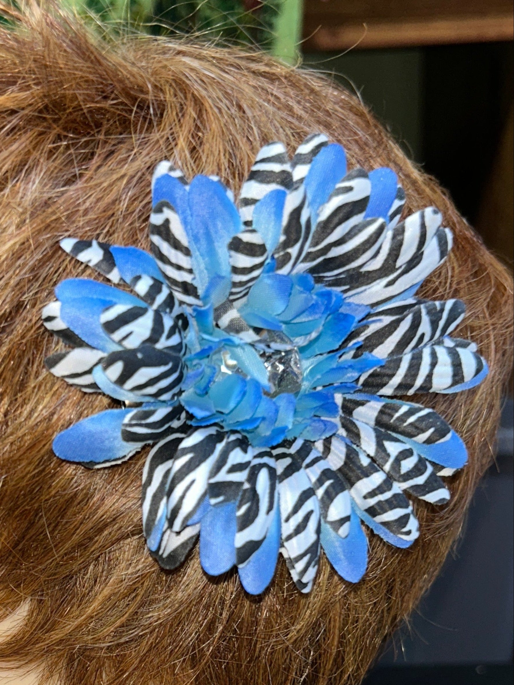 Mannequin head with a blue and black flower hair accessory on a textured surface.