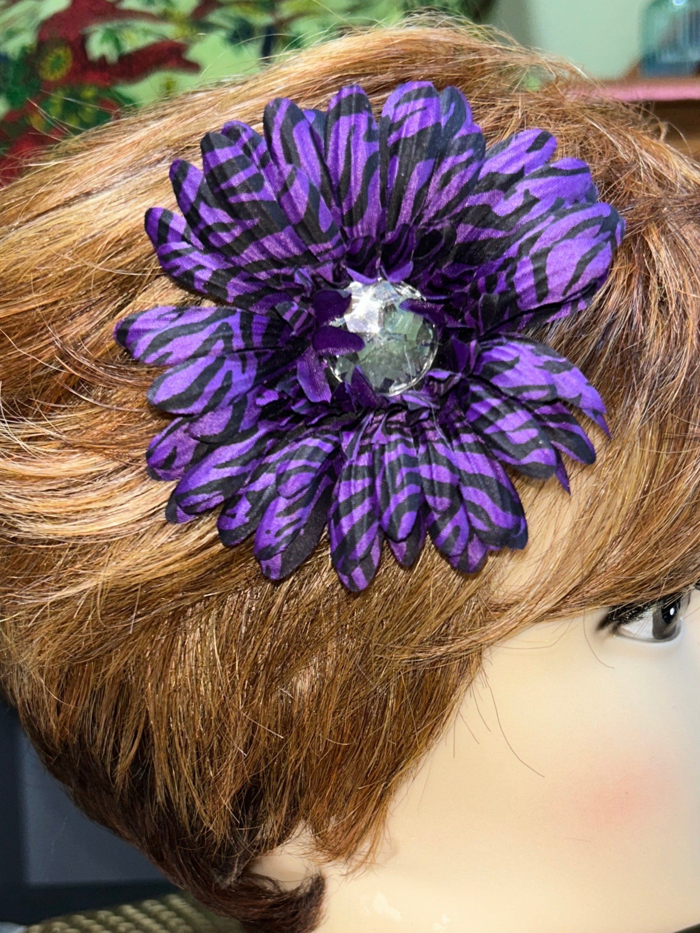 Mannequin head with brown hair and purple flower accessory, blurred indoor background